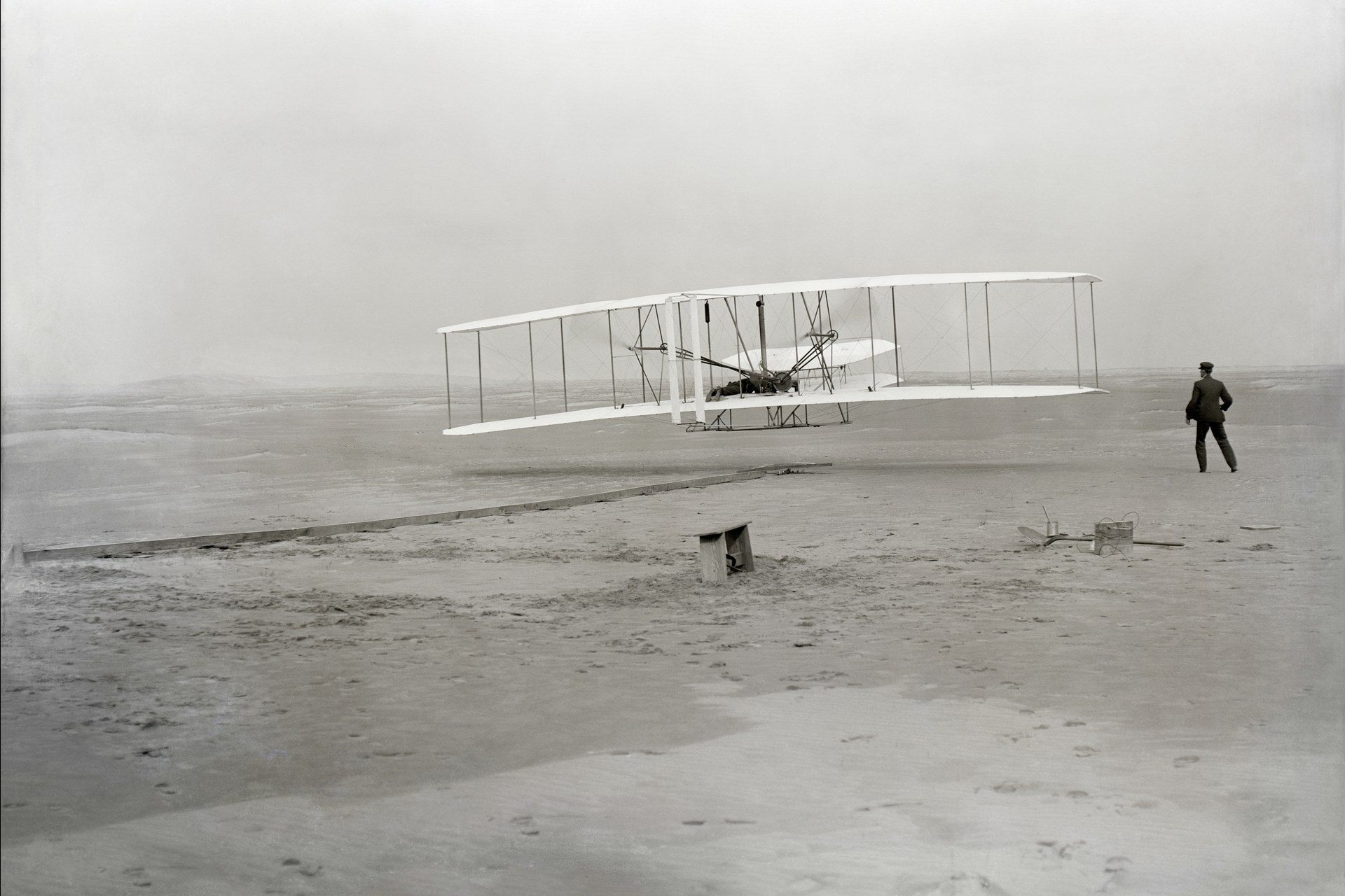 Le premier vol motorisé des frères Wright à Kitty Hawk, 17 décembre 1903 : Orville Wright dans le Flyer en l'air, Wilbur Wright courant à côté sur le sable