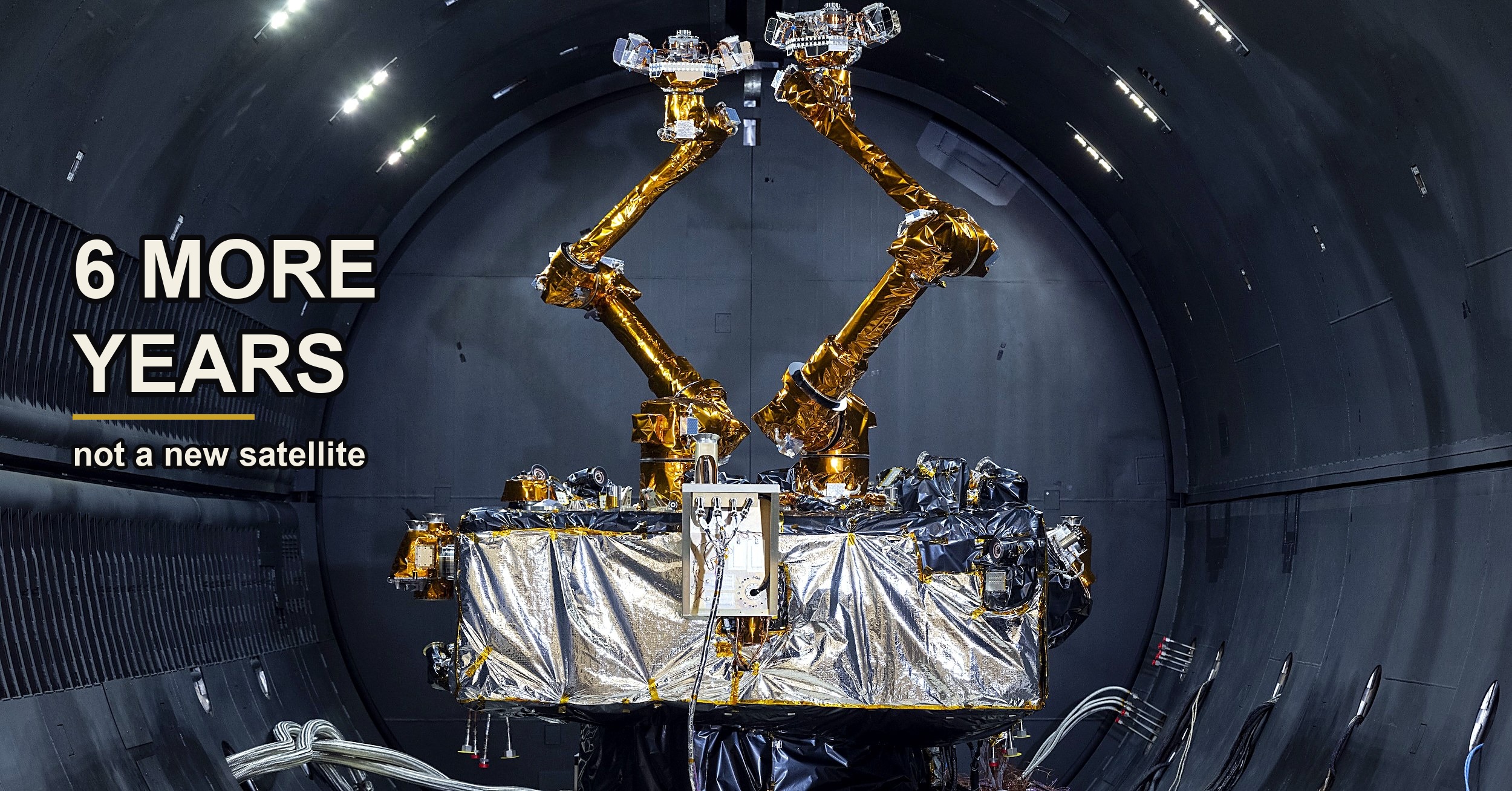 The Mission Robotic Vehicle's two gold-foiled robotic arms raised in a V inside a dark test chamber.