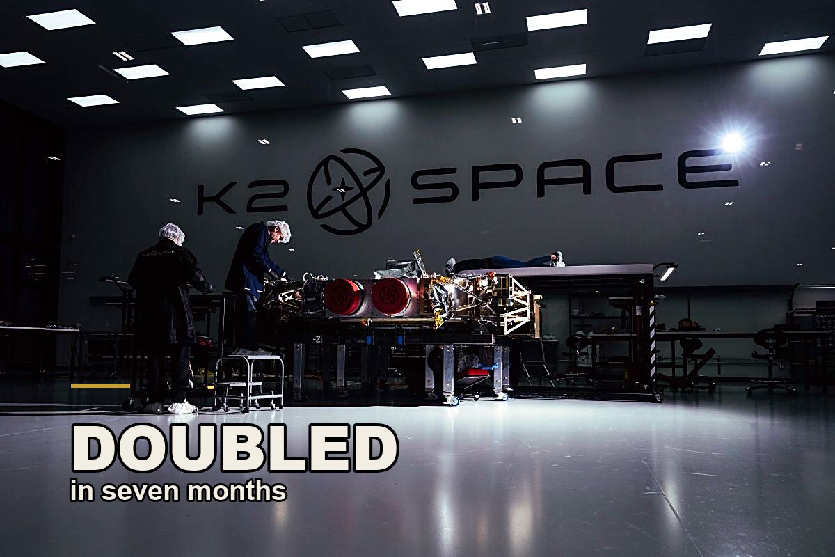 Two engineers build a large satellite on the K2 Space factory floor in Torrance, under the K2 Space logo