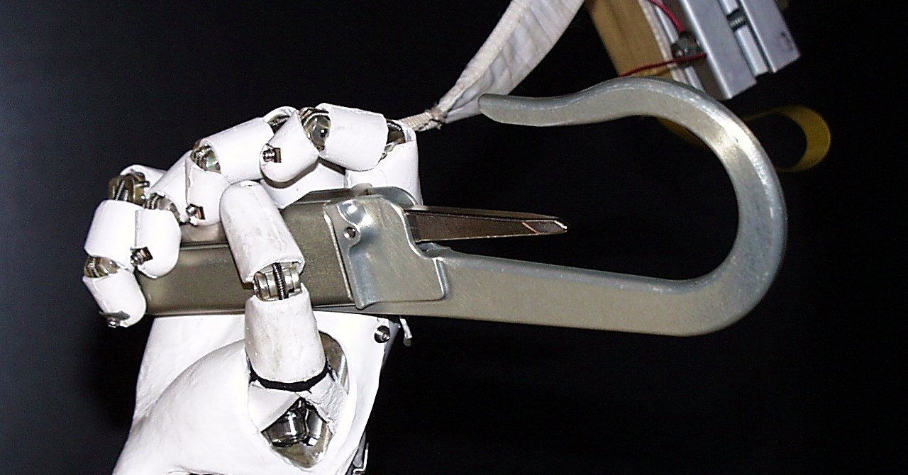 A white dexterous robotic hand grasping a metal tether hook against a black background during evaluation testing.